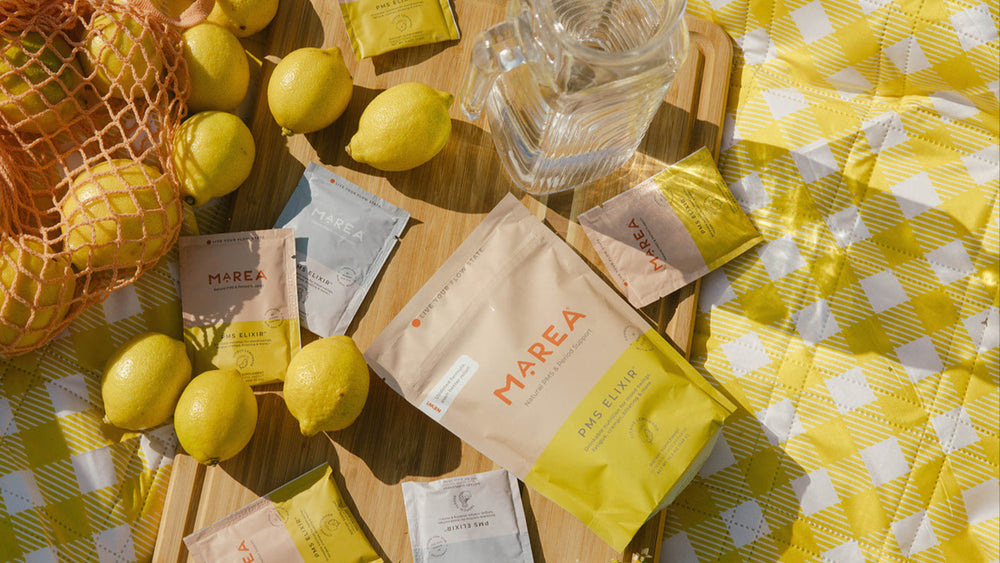 Table setting with lemons, Marea tea bags, and a pitcher on a yellow checkered tablecloth.